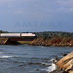 Train moving along the edge of a waterway, 1980s.